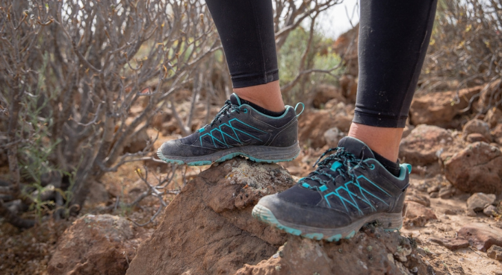 Woman wearing sneakers stands on boulder.